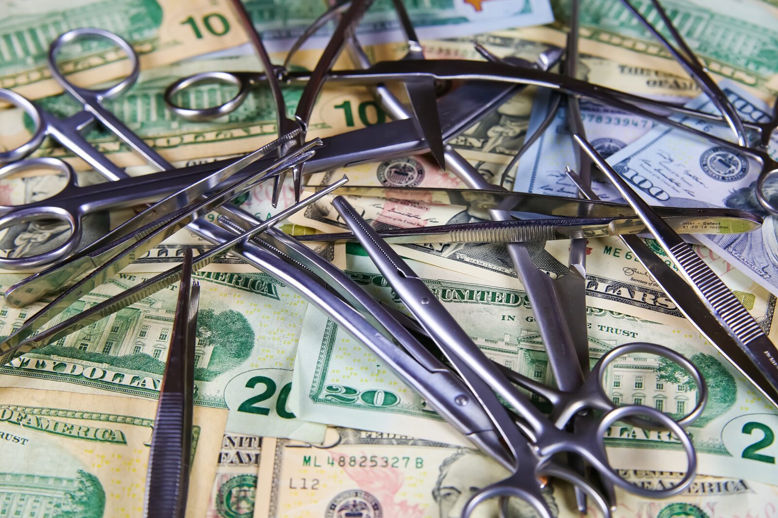 Medical forceps and tweezers lying on dollar bills