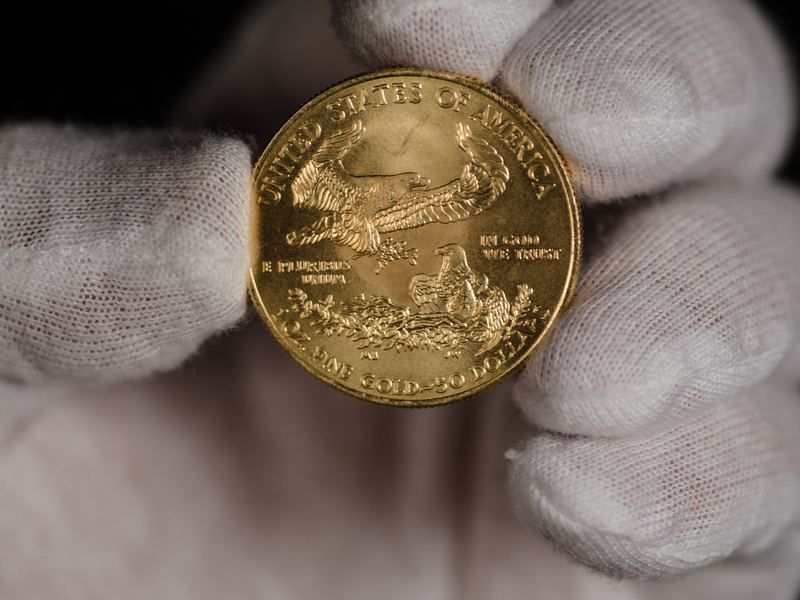 One troy ounce gold American Eagle coin held in a white glove